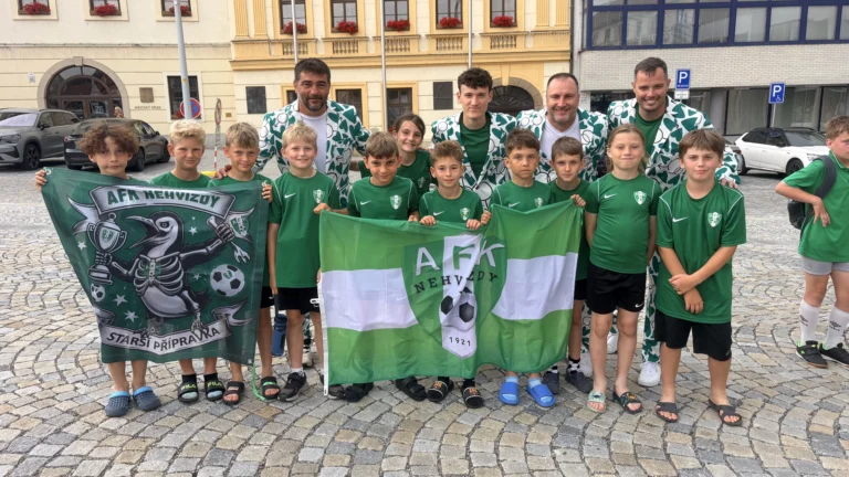 Mladí fotbalisté AFK Nehvizdy se svými trenéry pózují na náměstí v Třebíči. Děti drží klubovou vlajku a transparent starší přípravky.